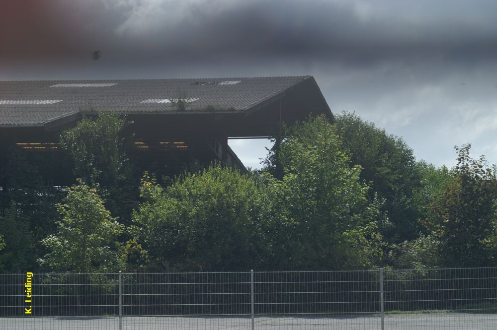 Blick durch den Zaun bei der Dreherei der GLOBUS Gummiwerke auf die Tonlagerhalle der Ziegelwerke.