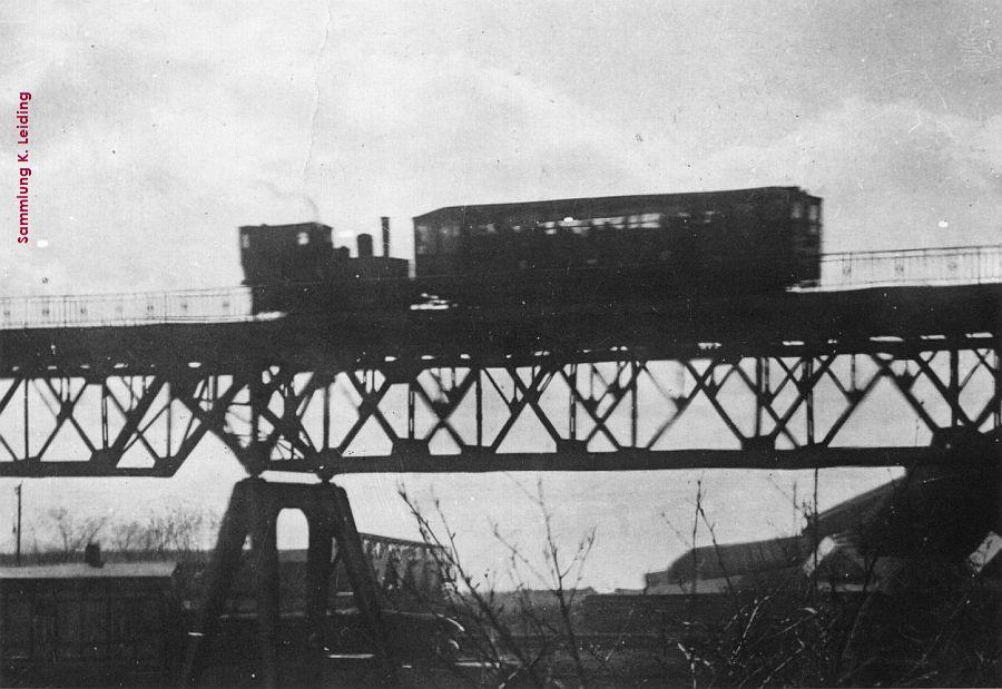 Dampflok schiebt einen Hochbahnwagen.